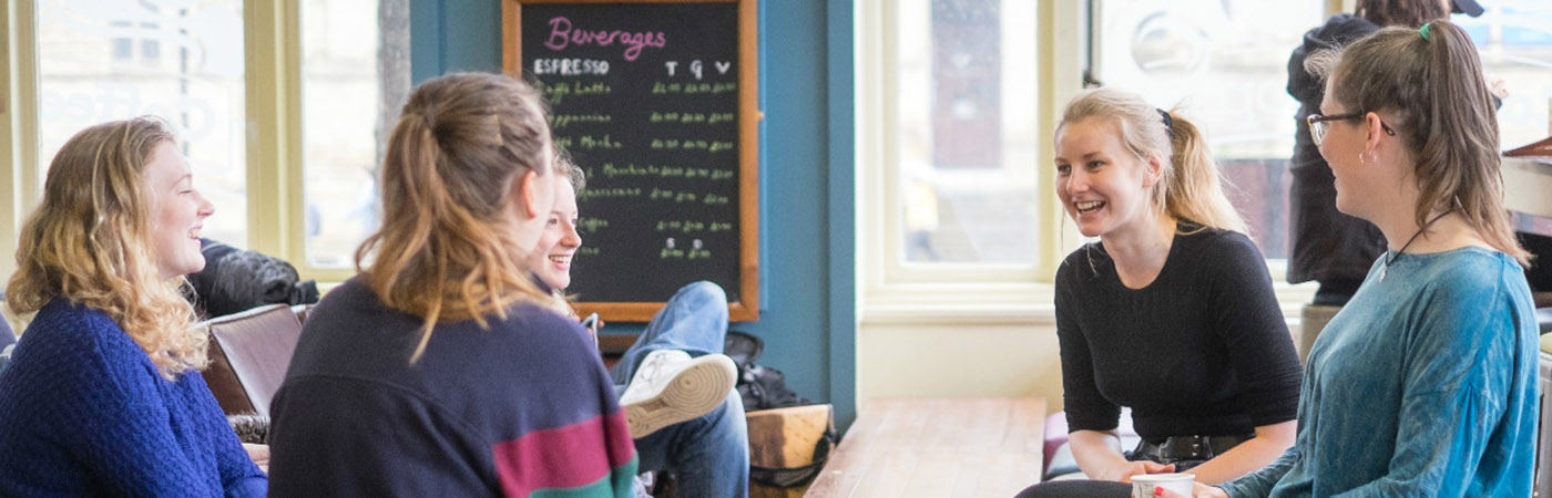 Groups of people sat at a table in a coffee shop talking